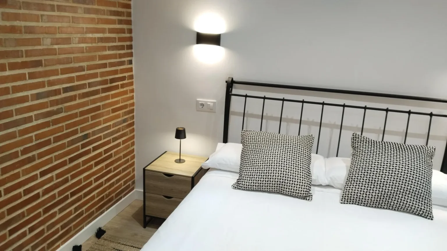 Habitación con pared de ladrillo visto y cama de forja